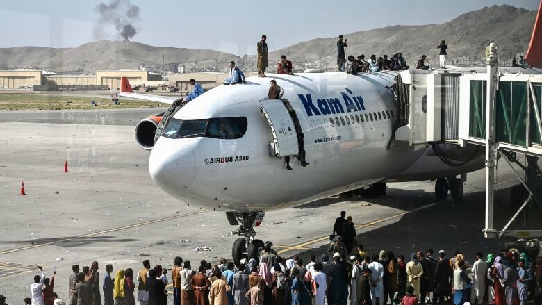 A plane with KAM AIR written on it sits on a tarmac. people are crowded around it - some are standing on top of it. 