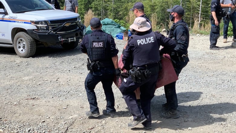 Police officers carry away someone in what appears to be a box of some sort, as others look on.