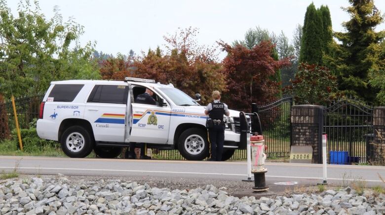 A police vehicle lies parked outside a property gate, with two officers nearby.