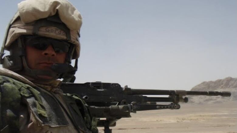 A soldier holds an automatic rifle in the desert.