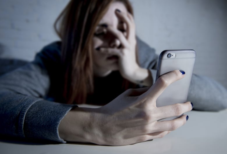 A young woman holding a cellphone closes her eyes and puts her other hand over her face.