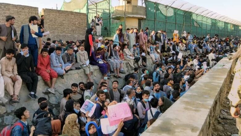 People sit on walls, crowded together, on an airfield.