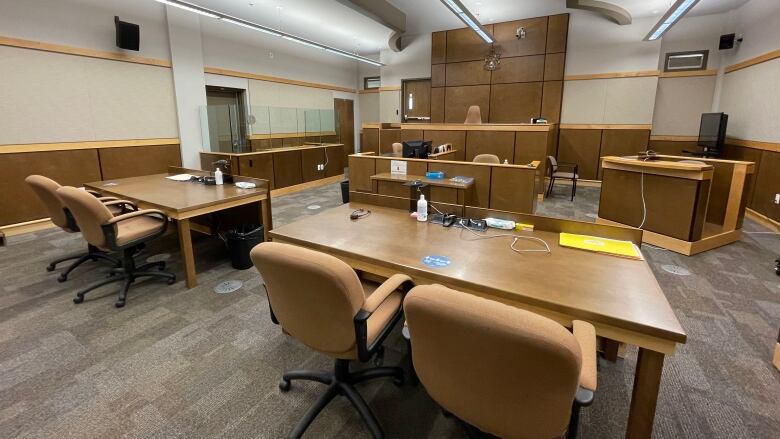 A courtroom with two tables with chairs in the foreground, a dais in the background where the judge sits, a witness stand to the right and a prisoner's box on the left.