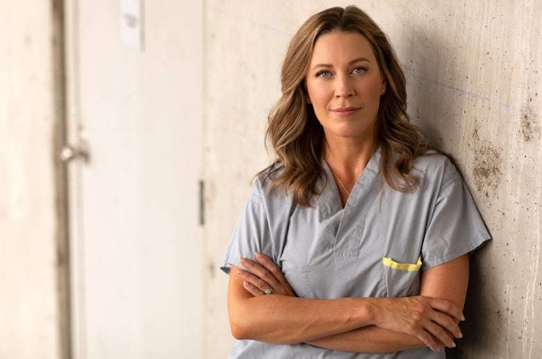 Dr. Katherine Smart is wearing grey scrub and looking directly into the camera as she leans against a wall with her arms crossed