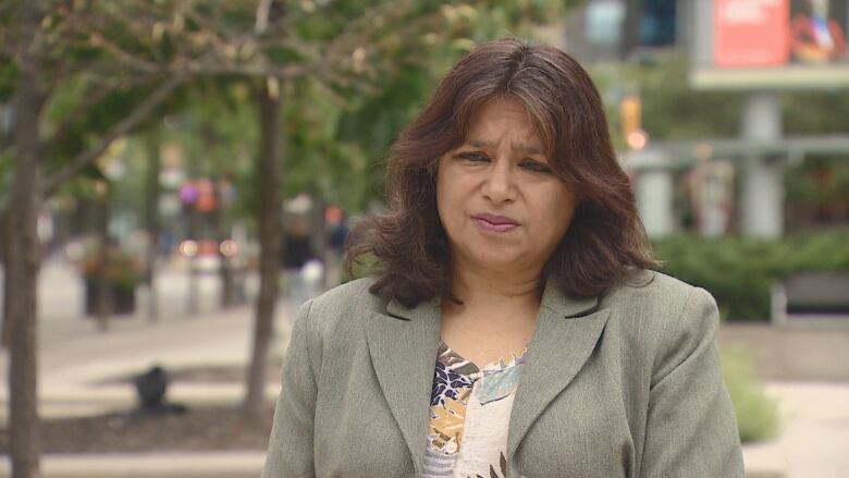 A woman stands outside in a suit jacket. 