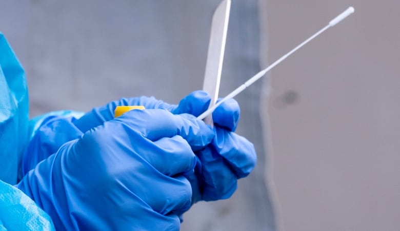 A nurse wearing blue gloves handles a COVID-19 test swab. 