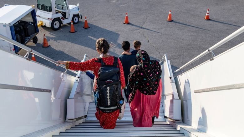 Two women and two men dressed in traditional clothes descend an airport staircase onto the airport tarmac.