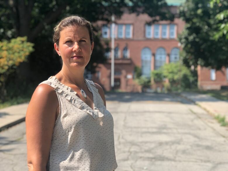 A woman looks at the camera. A school is in the background.