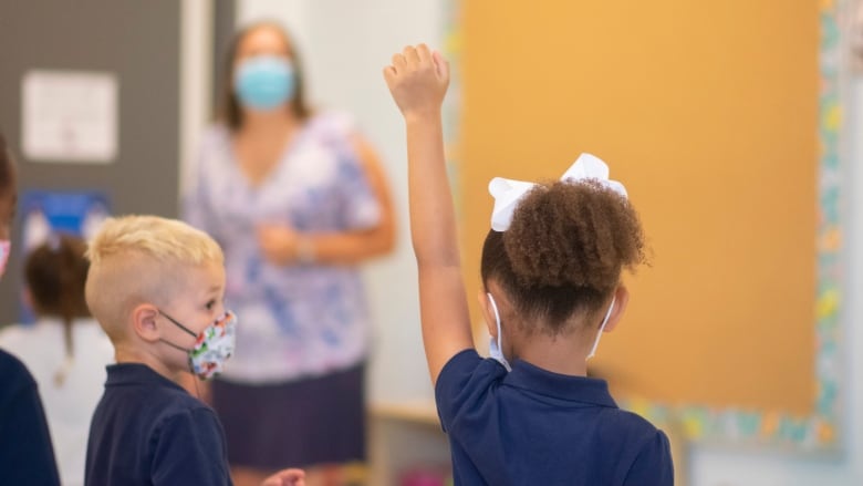 A kindergarten student wearing a mask at Sts. Peter & Paul Catholic Elementary School in Hamilton raises her hand in class. 