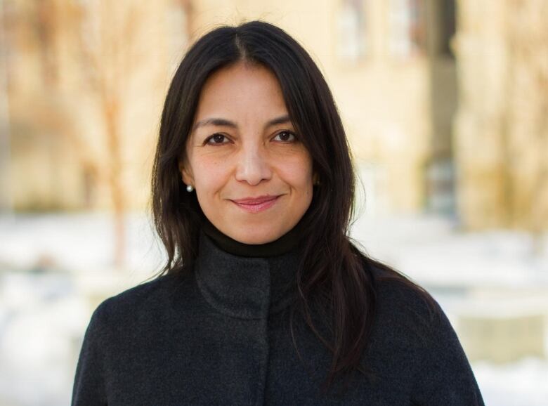 Castillo is wearing a dark grey jacket and smiling. She's outside and trees and snow can be seen behind her.