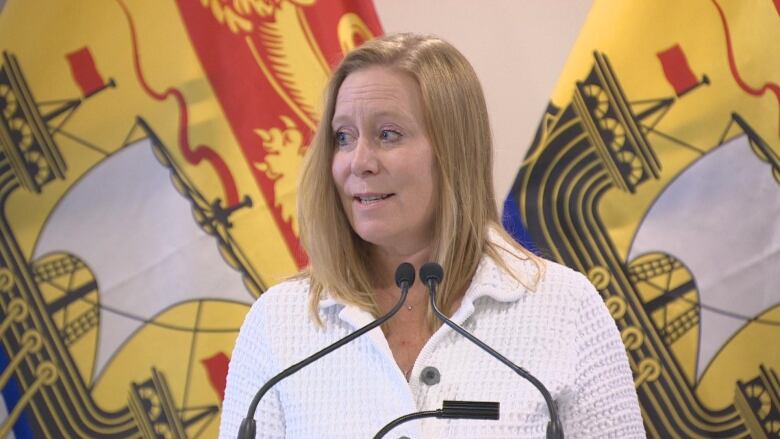 Woman standing in front of New Brunswick flags standing at a podium.