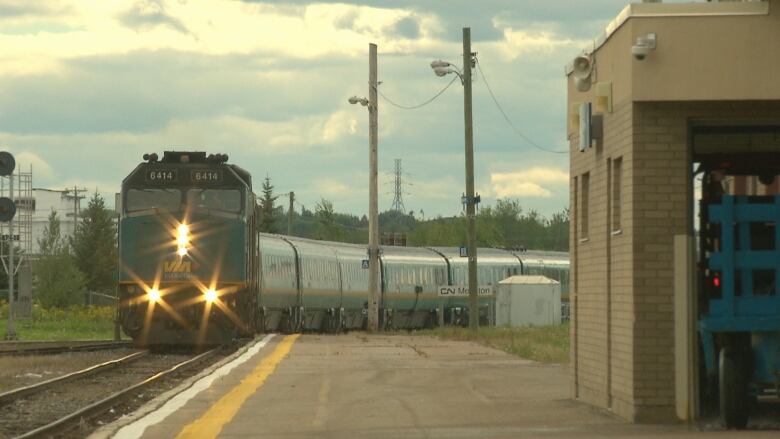 A green train on a track with the words Via Rail written on the front. It is driving up toward a station. 