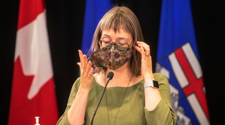 Dr. Deena Hinshaw is taking off a mask as she prepares to speak at a lectern during a news conference.