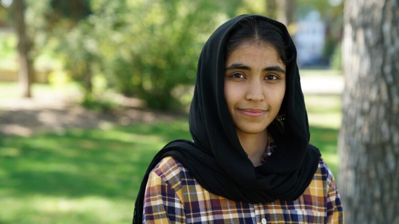 A young woman wearing a black headscarf smiles at the camera.