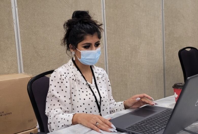 A woman wearing a blue face mask sits in front of a laptop computer.