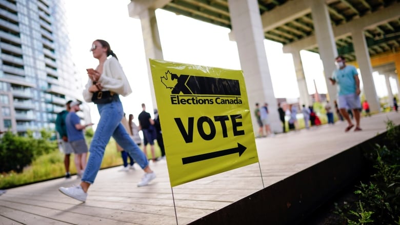 A woman walks along a boardwalk past a sign for voting.