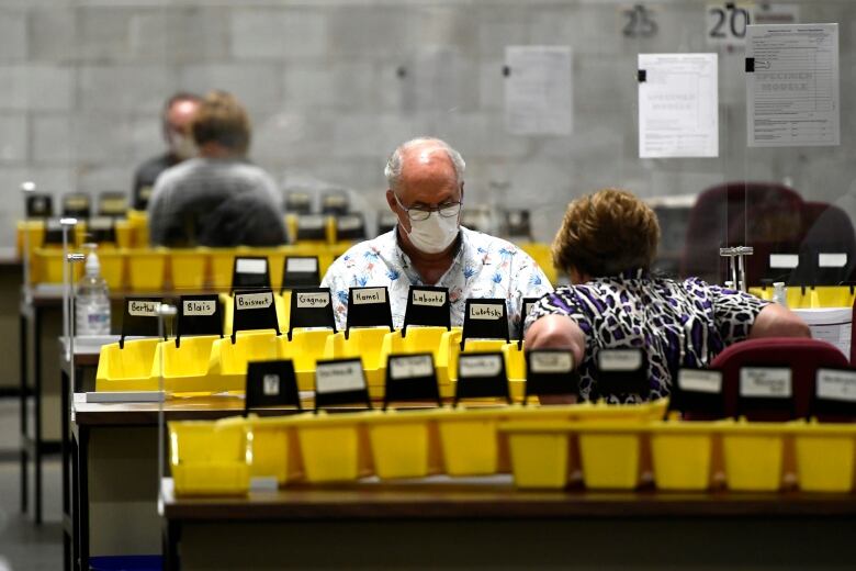 A man with grey hair sits at a table where special ballots are being counted. 