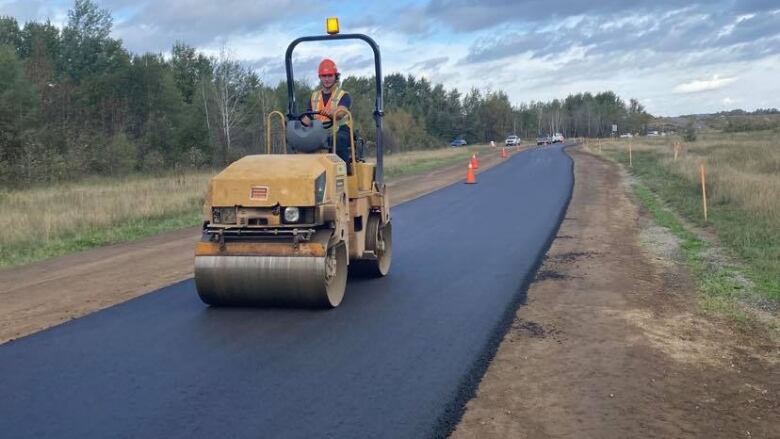 A steamroller drives across a freshly paved patch of asphalt. 