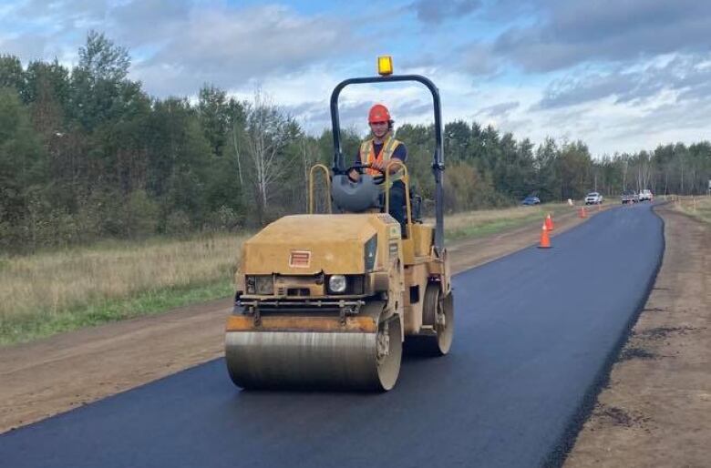 A steamroller drives across a freshly paved patch of asphalt. 