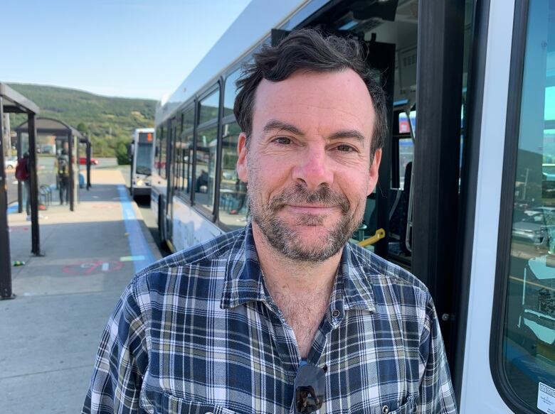 Man with beard and short brown smiles in front of a bus.