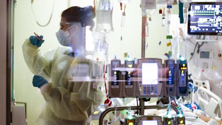 A nurse can be seen, behind IV bags and monitors,  working in an intensive care unit