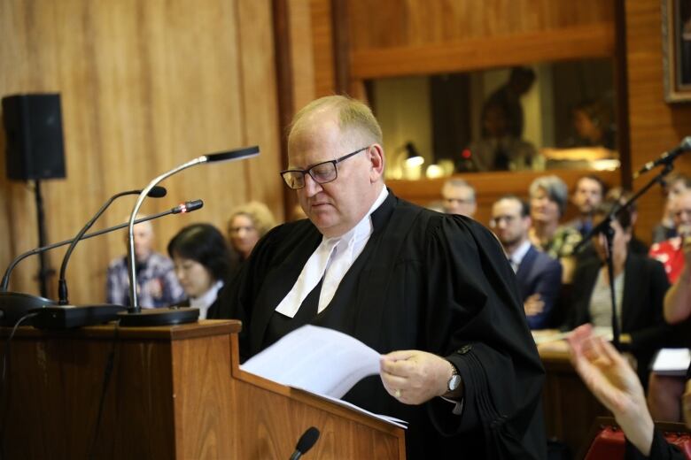 A lawyer wearing a black robe, standing behind a podium. 