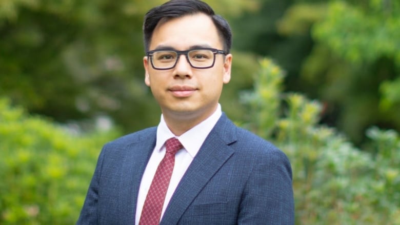 An East Asian man wearing a suit and red tie looks straight at the camera.