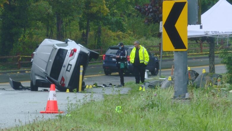 A large SUV is seen upturned on a road, with two officers looking at it pensively.