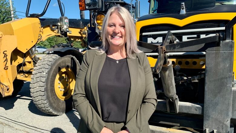 Nova Scotia Public Works Minister Kim Masland smiles in front of yellow and black construction vehicles.