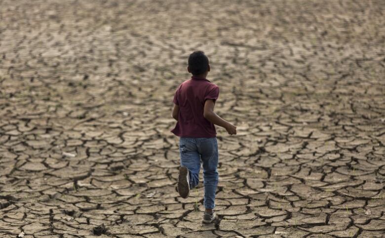 A young boy runs across extremely dry soil.