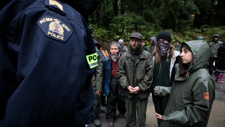 Activists in raincoats look to a Mountie.