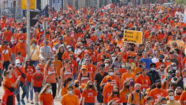 Sea of people all wearing orange shirts march together. One person is holding up an orange sign that reads 