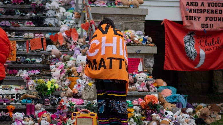 A person stands in front of steps filled with children's toys and clothes. The person is wrapped in a banner.