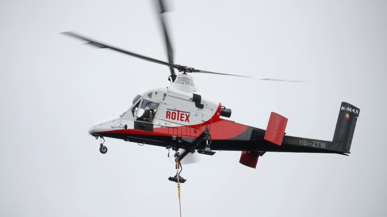 A Kaman K-Max K-1200 red and white helicopter in flight.