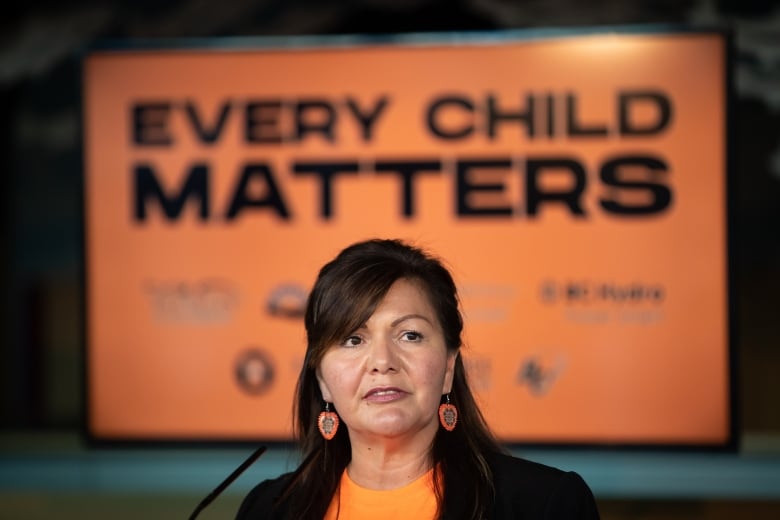 A woman speaks in front of a banner reading 'Every Child Matters.'