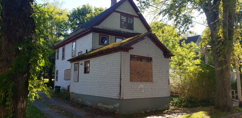 White house with boarded-up windows and moss on the roof.