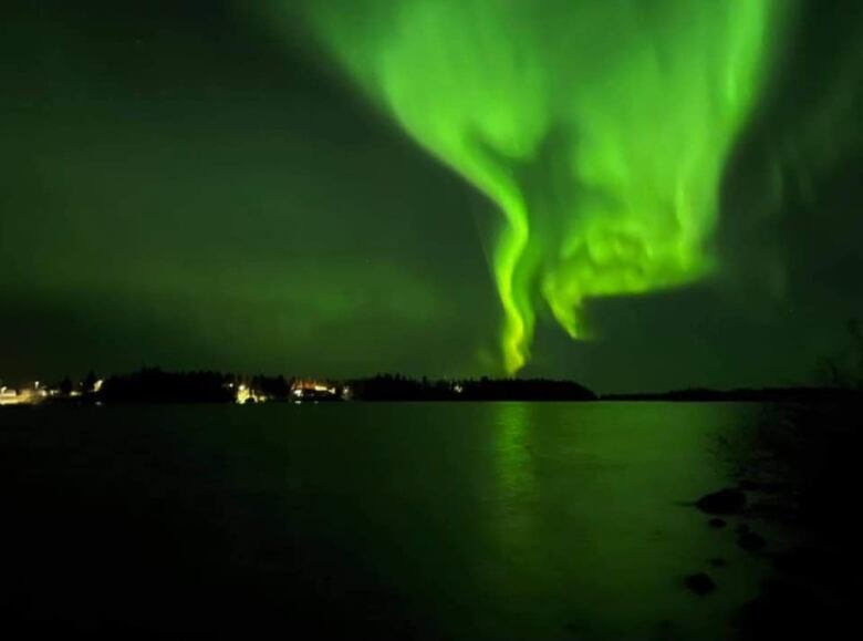 Swirls of green light brighten the sky over a lake and land in the distance.