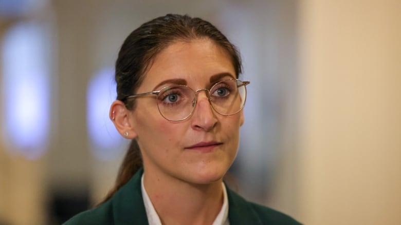 A woman with a ponytail and glasses, white shirt and dark suit jacket.