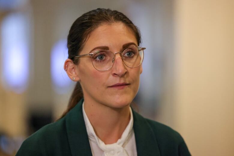 A woman with a ponytail and glasses, white shirt and dark suit jacket.