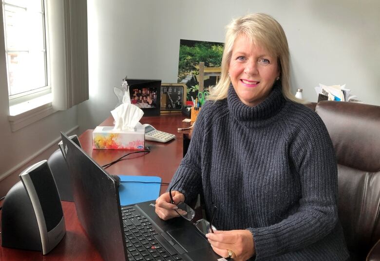 A woman in a sweater sits at her computer desk.