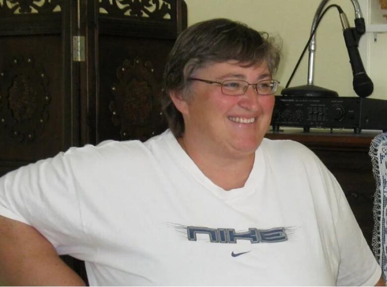 A woman wearing glasses and a white nike shirt looks off camera. She is smiling. 