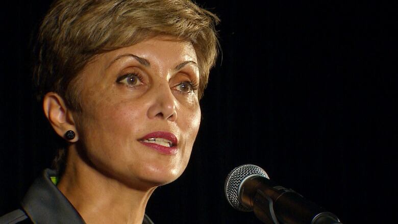 A close-up shot of a woman with short hair. She is seen sporting red lipstick and speaking into a mic in this photo.