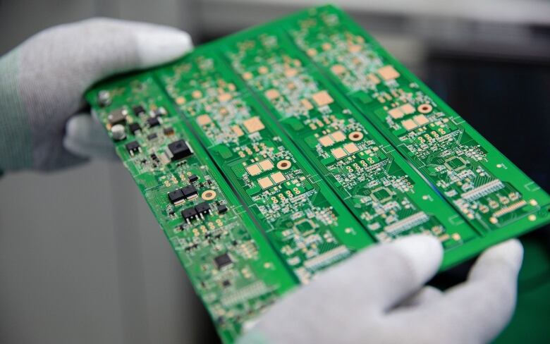 White gloved hands hold a large green circuit board with semiconductors