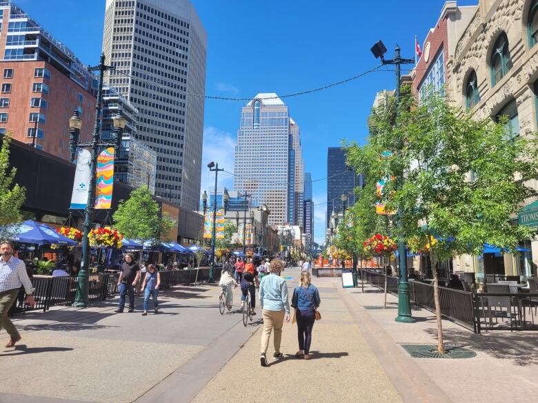 People walk down the street on a bright sunny day. Tall downtown buildings can be seen around them.