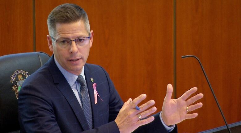 A headshot of former mayor of Winnipeg, Brian Bowman, sitting in city hall behind a microphone.