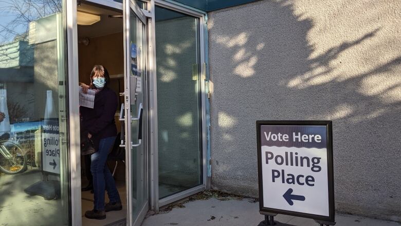 A sign out the front of a polling place in Whitehorse. A woman in a facemask is visible through an ajar door. 