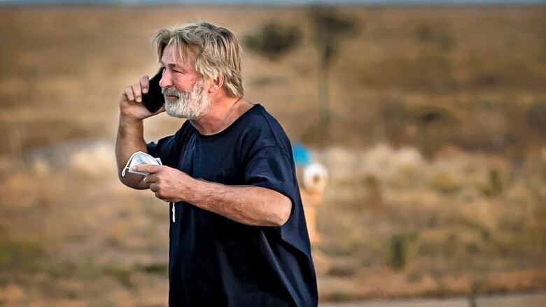 A bearded man standing in a parking lot speaks on a cellphone.