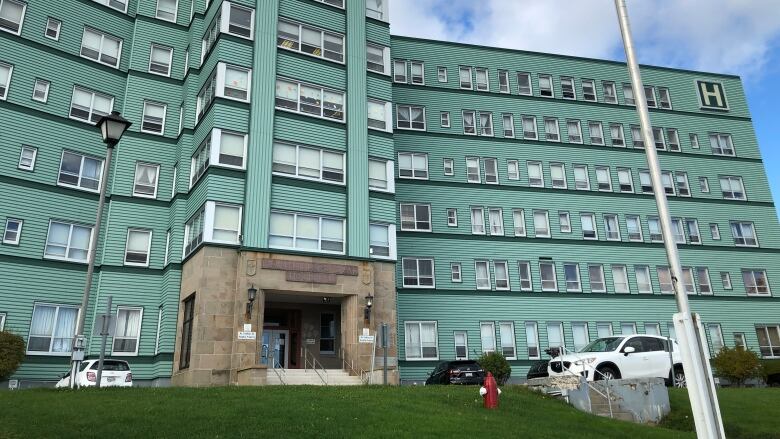 A Canadian flag blows in the wind in front of a green, six-storey hospital building.