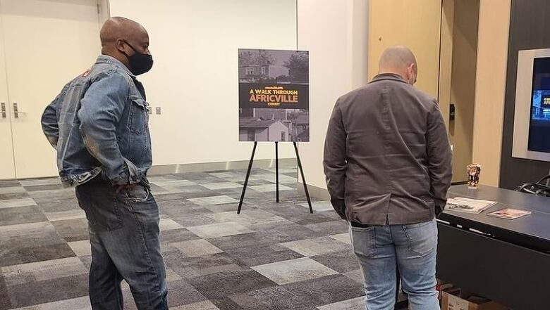 Two men standing near a sign that reads 