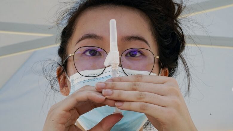 A woman wearing a medical mask holds a needle in preparation for an injection.